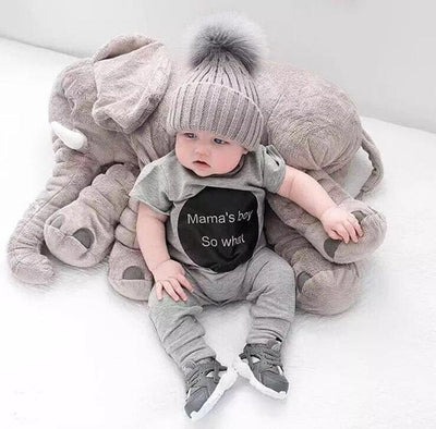 Baby in a gray outfit with 'Mama's Boy So What' shirt surrounded by large plush toys on a white background