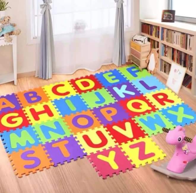 Colorful alphabet foam mats on a wooden floor in a room with books and toys.