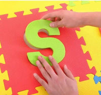 Colorful foam puzzle mat with a letter 'S' being held by a hand
