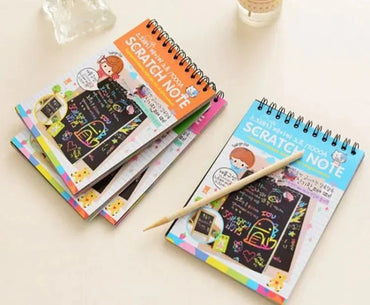 Colorful spiral-bound scratch note books with a wooden stick on a light surface