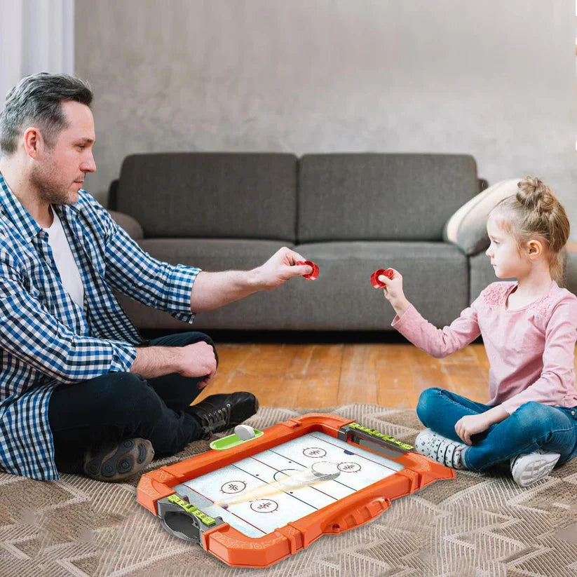 Man and child playing with a hockey game on an orange board in a living room.
