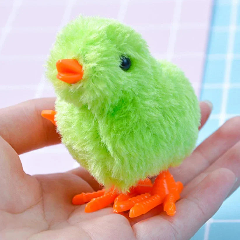 Small green plush toy chick with orange feet and beak held in a hand against a light background