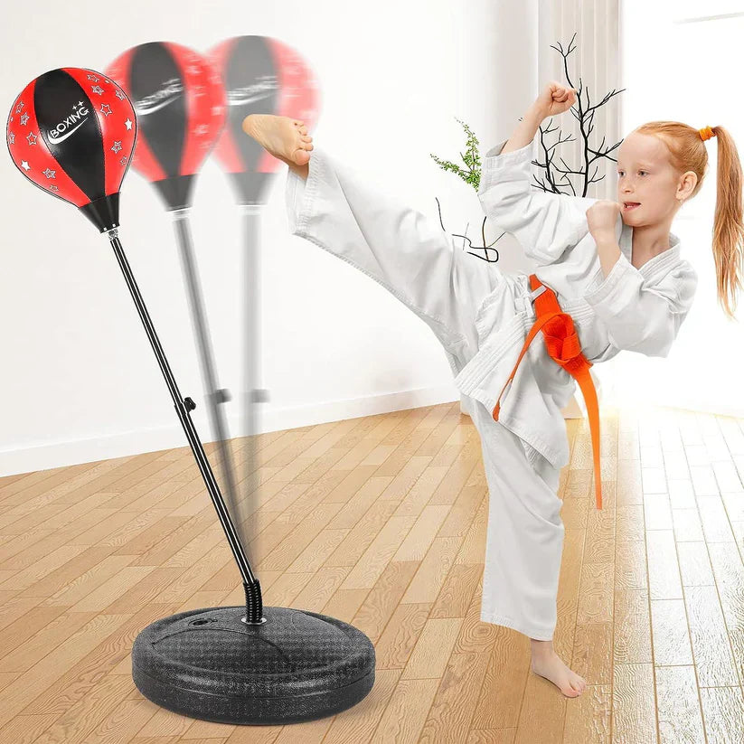 Child in martial arts uniform practicing a kick on a standing punching bag indoors.