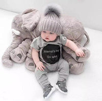 Baby in a gray outfit with 'Mama's Boy So What' shirt surrounded by large plush toys on a white background